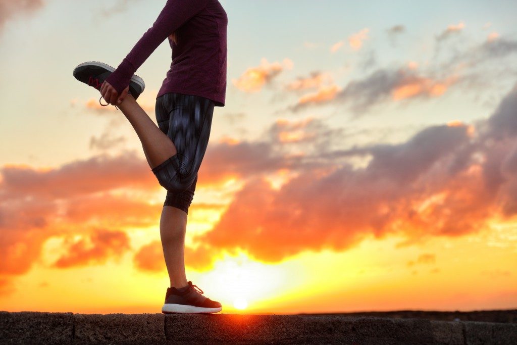 woman stretching leg muscle preparing for sunset trail run in outdoor summer