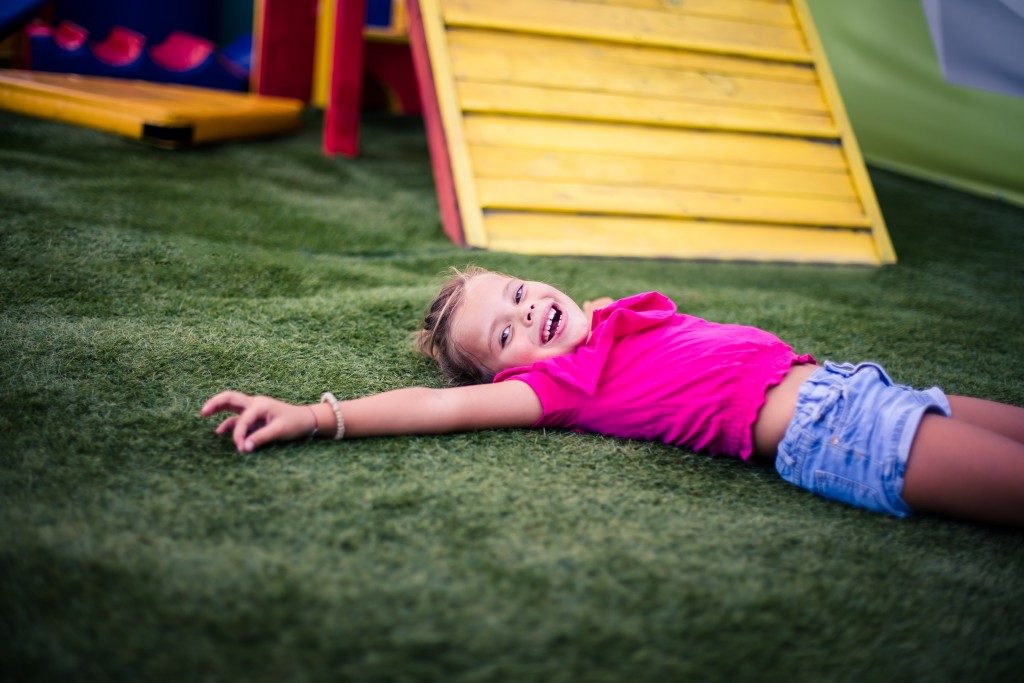 Child laying on the grass next to playground